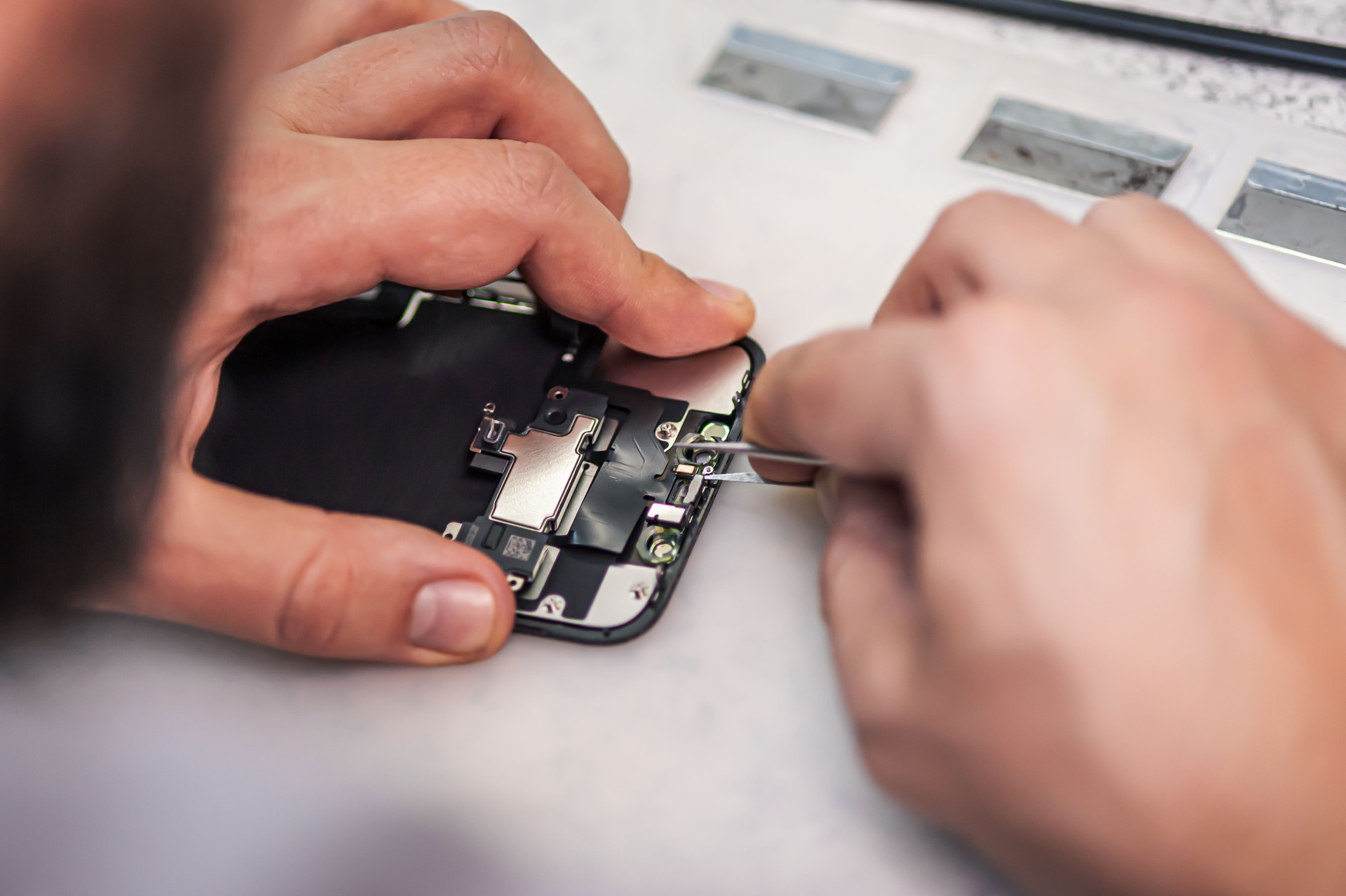 Technician repairs smartphone, uses tweezers as tool in electronics workshop